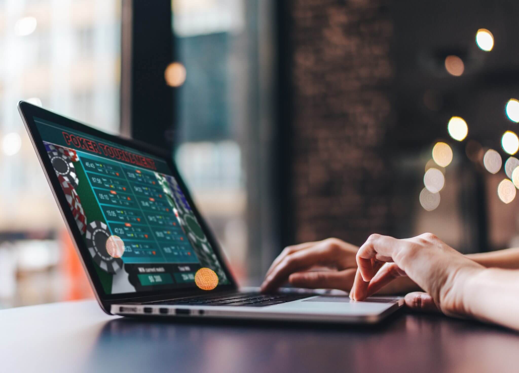 Person using a laptop displaying an online poker tournament interface, with hands on the keyboard and a blurred background.