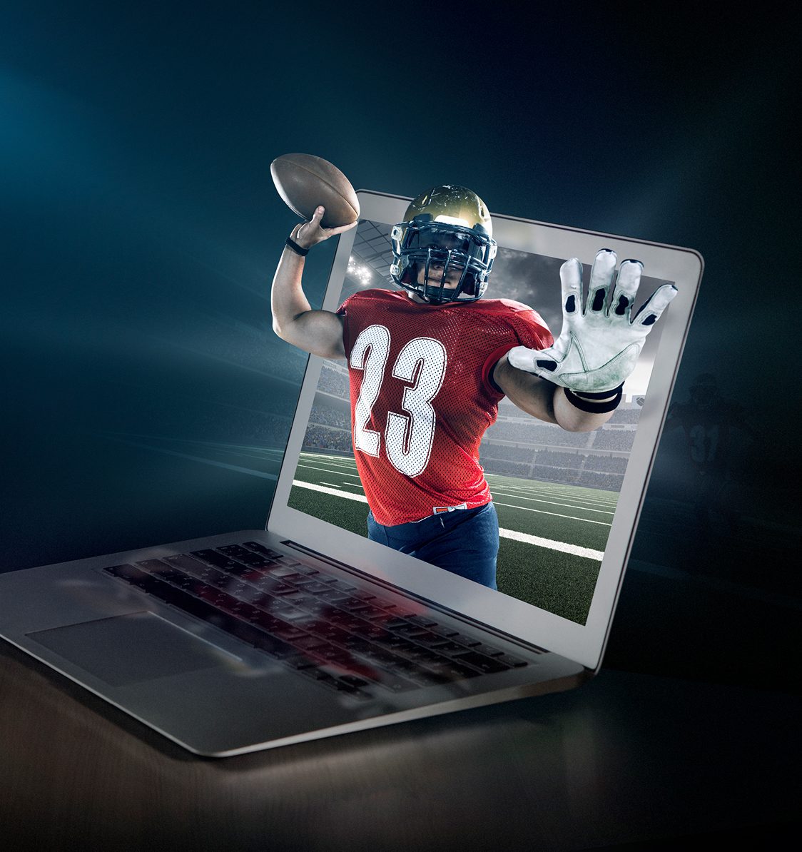A football player in a red jersey appears to jump out of a laptop screen while holding a football, with a stadium in the background.
